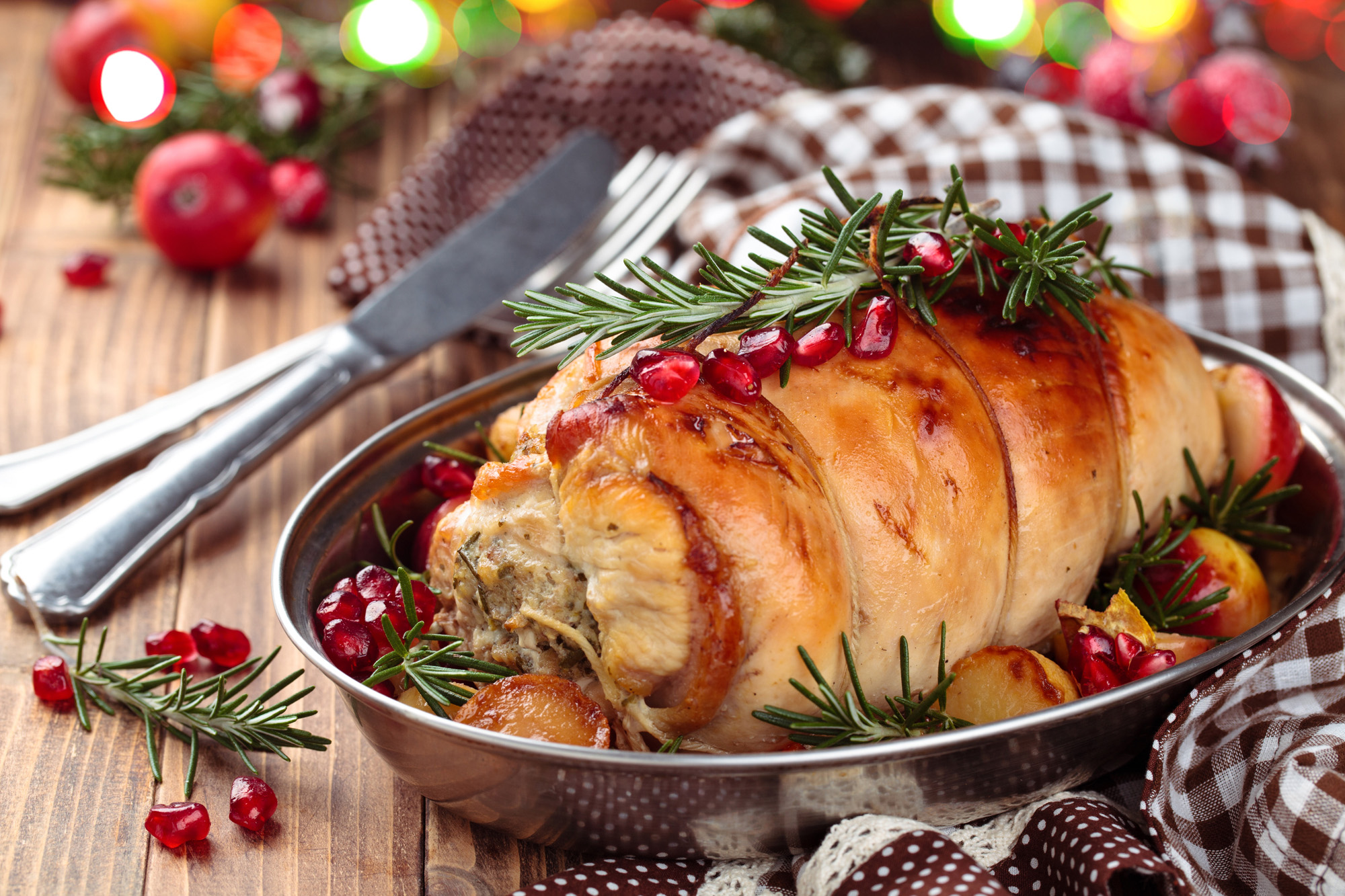 Stuffed turkey breast with baked vegetables and spices against holiday lights background.